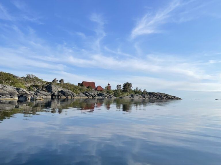 Kallioinen saaristomaisema, punakattoisia rakennuksia ja tyyni meri
